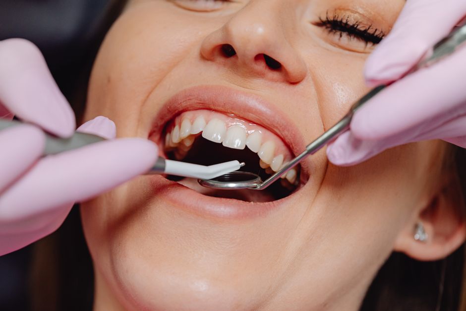 pexels-photo-6627519-6627519 Smiling woman at dentist with tools for dental exam, highlighting dental care.
